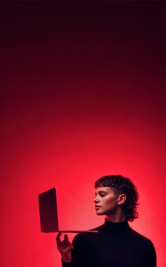 Una joven con cabello corto sostiene una laptop delgada con sus dedos a la altura de su cabeza para revisar las opciones de diplomados en línea de la Universidad Iberoamericana.