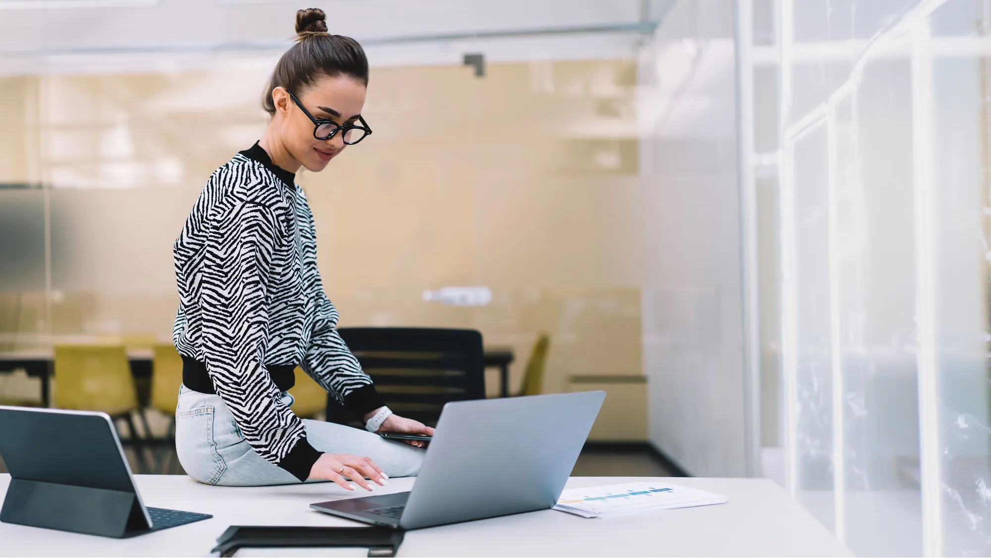 Un profesionista con ropa semiformal dentro de una oficina sentada sobre uneescritorio, estudia su diplomado online de la Universidad Iberoamericana.