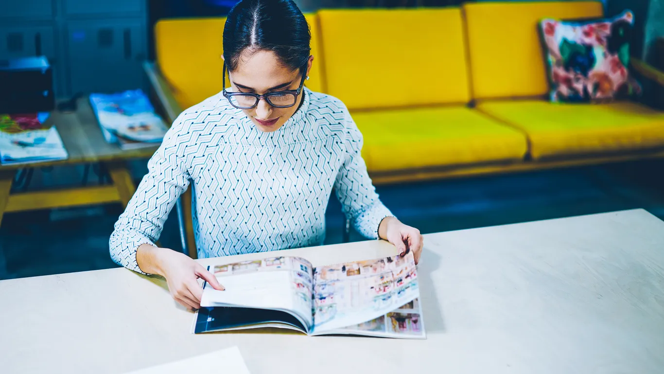 Una mujer revisa en una revista dentro de una biblioteca diplomados con validez universitaria.